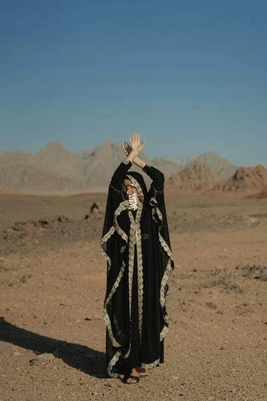 a person standing in the middle of a desert, an album cover, by Maryam Hashemi, symbolism, waving robe movement, press shot, on a far planet, mountains in distance