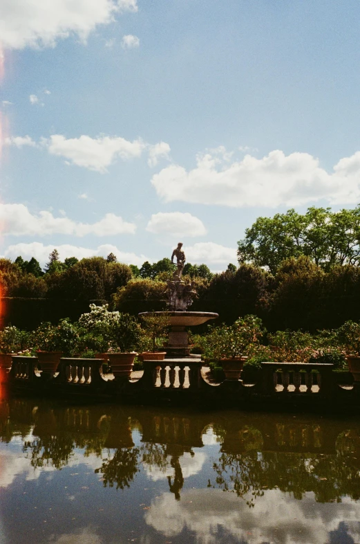 there is a fountain in the middle of a pond, a statue, inspired by Serafino De Tivoli, pexels contest winner, panoramic view, grainy low quality, lush surroundings, overlooking