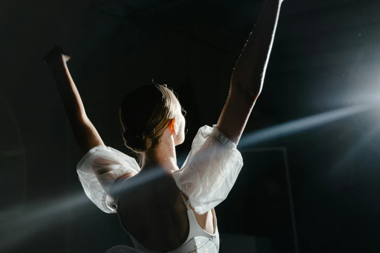 a woman in a white dress with her arms in the air, pexels contest winner, light and space, theatrical lighting, sydney sweeney, with backlight, female dancer