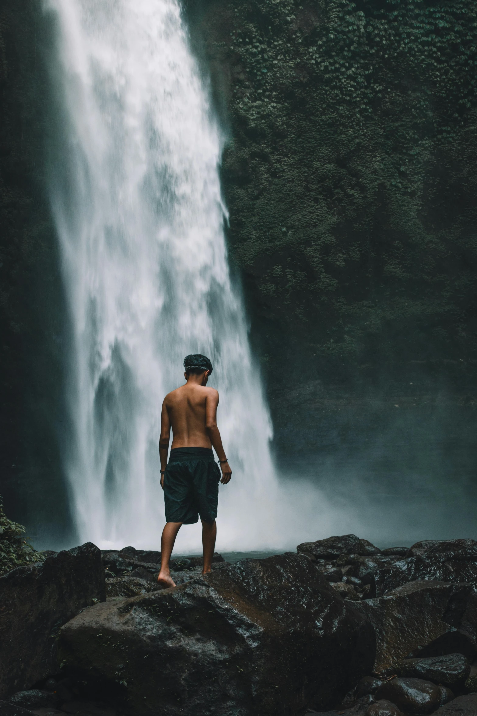 a man standing in front of a waterfall, pexels contest winner, loin cloth, facing away, teenage boy, bali