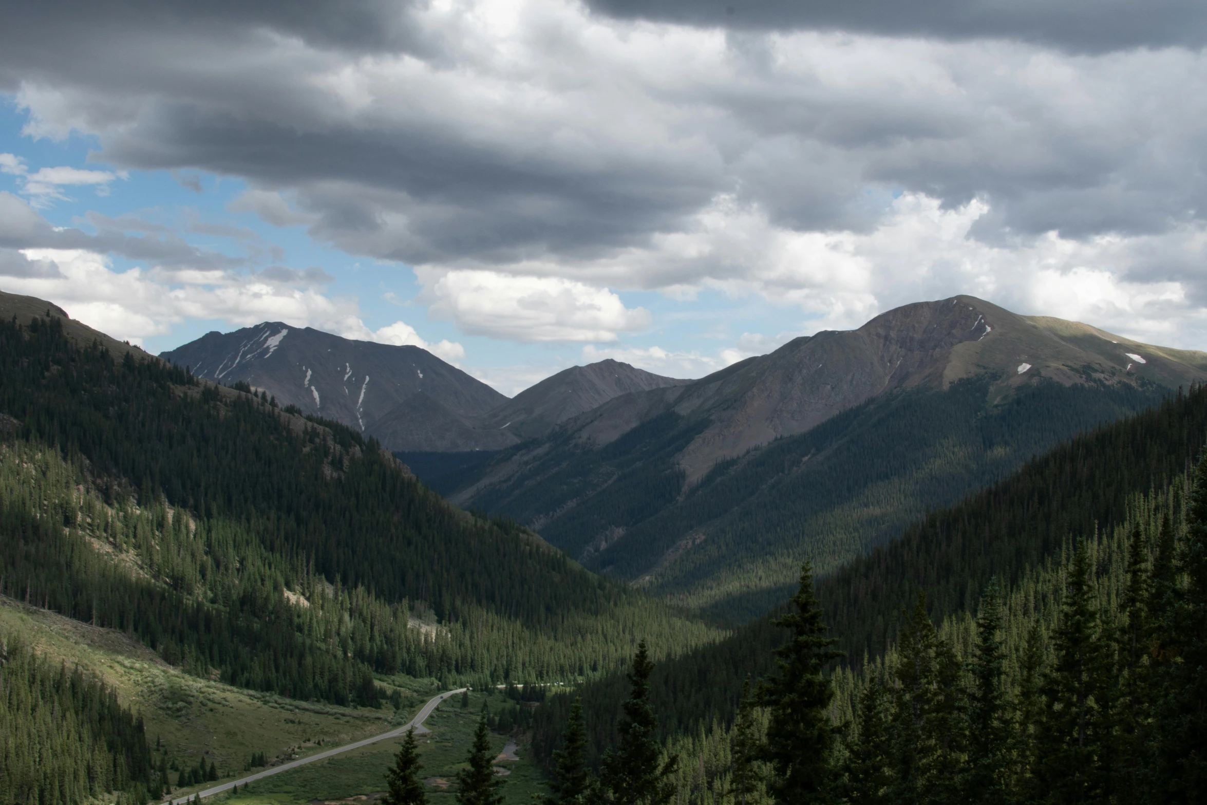 a view of the mountains from the top of a hill, by Emma Lampert Cooper, unsplash contest winner, colorado, gray clouds, highway 5 0, lush forest in valley below