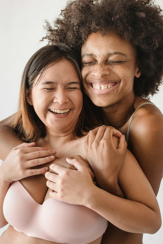 two women hugging each other in front of a white background, a photo, trending on pexels, belly button showing, mixed-race woman, cervix awakening, smiling woman