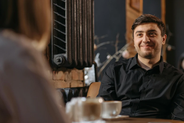 a man in a black shirt sitting at a table, pexels contest winner, smiling at each other, hasbulla magomedov, aussie baristas, avatar image