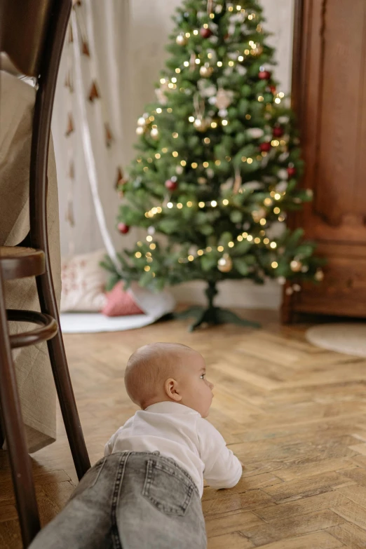 a baby laying on the floor in front of a christmas tree, a picture, by Julia Pishtar, pexels contest winner, man sitting facing away, decoration around the room, gif, profile image