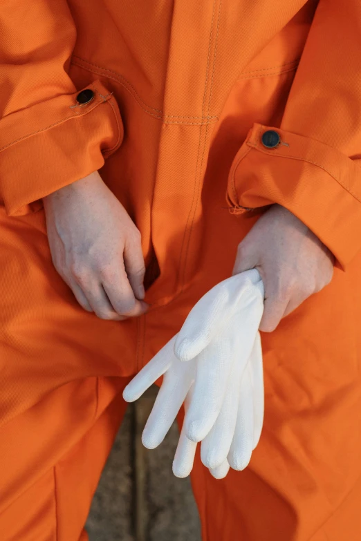 a person in an orange jumpsuit and white gloves, lined in cotton, zoomed in, white, medium-shot