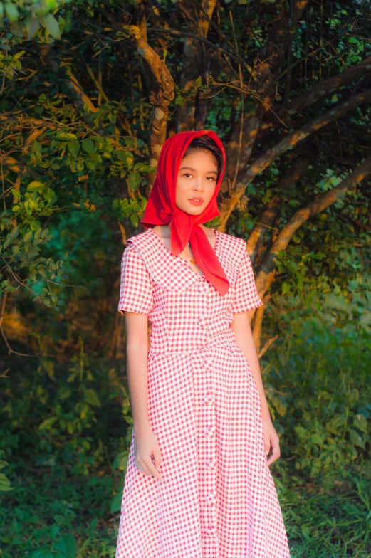 a woman standing in front of a tree wearing a red scarf, an album cover, by Cherryl Fountain, unsplash, cute checkerboard sundress, wearing a head scarf, in style of lam manh, 2 0 yo