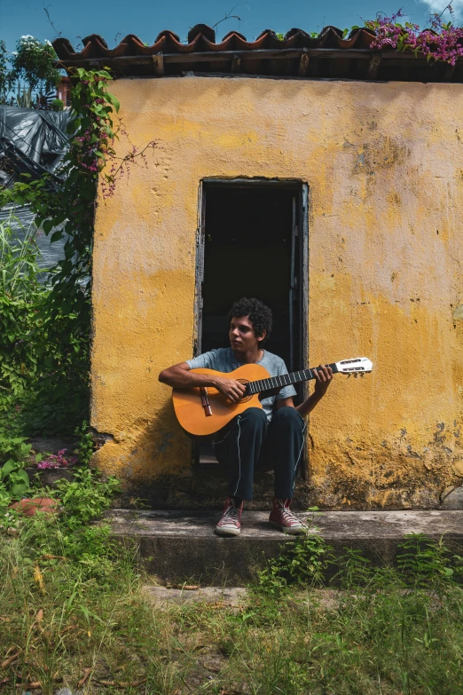 a man sitting in a doorway playing a guitar, an album cover, by Alejandro Obregón, pexels contest winner, on a village, jayison devadas, profile pic, square