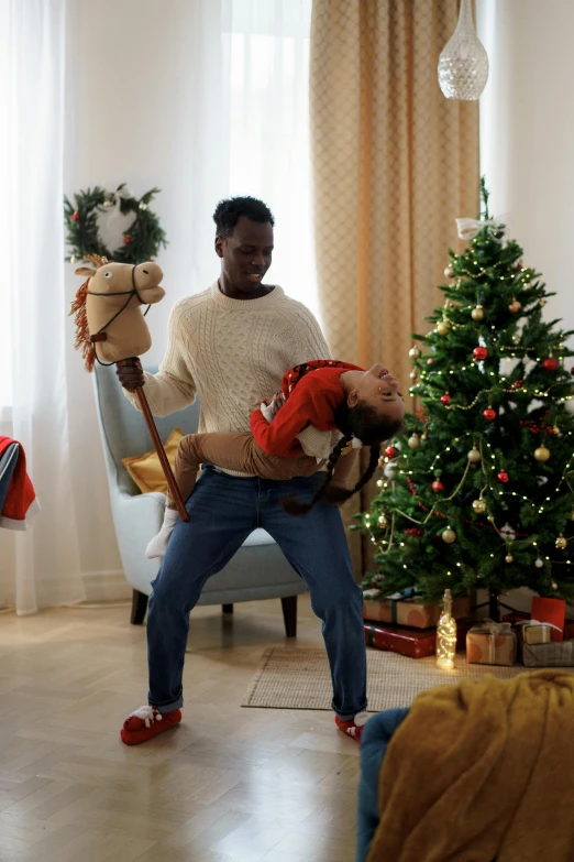 a man holding a child in front of a christmas tree, happening, choreographed fight scene, adut akech, thumbnail, home video