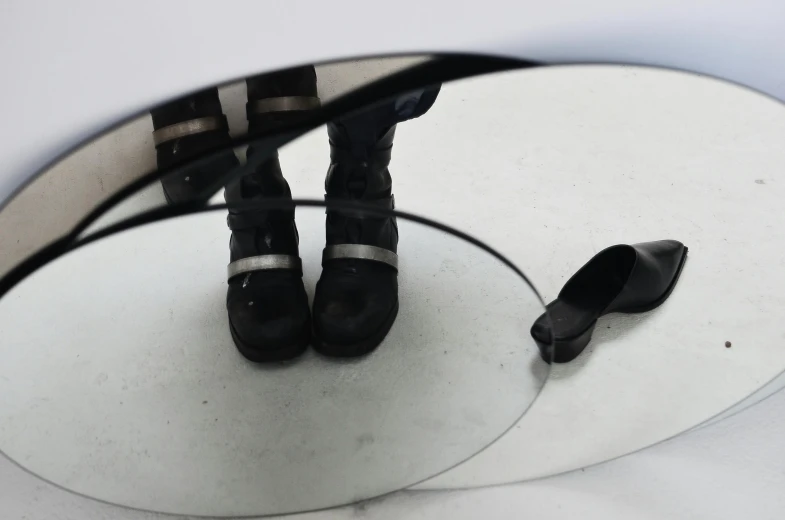 a person in high heels standing in front of a mirror, an album cover, by Nina Hamnett, unsplash, bauhaus, military boots, black and silver, black circle, reflections on a glass table