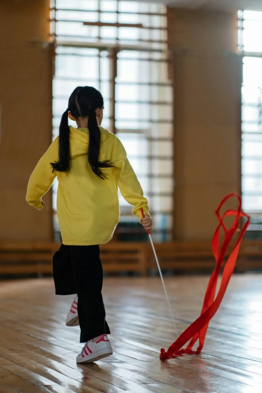 a girl in a yellow jacket is playing with a kite, gutai group, in a dojo, holding walking stick, promo image, red ribbon