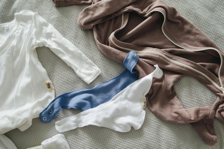 a pile of clothes sitting on top of a bed, by Nina Hamnett, unsplash, burnt umber and blue, blue'snappy gifts'plush doll, thin bodysuit, sleek hands