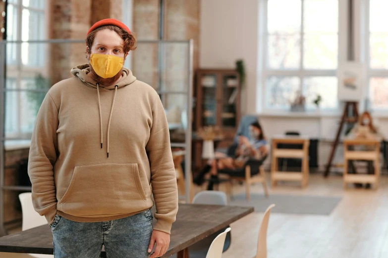 a man standing in a room with a yellow mask on his face, trending on pexels, girl wearing hoodie, on a wooden table, coworkers, non-binary