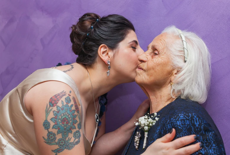 two women kissing each other in front of a purple wall, a tattoo, by Giuseppe Avanzi, pexels contest winner, nursing home, studio photo, old and young, wedding