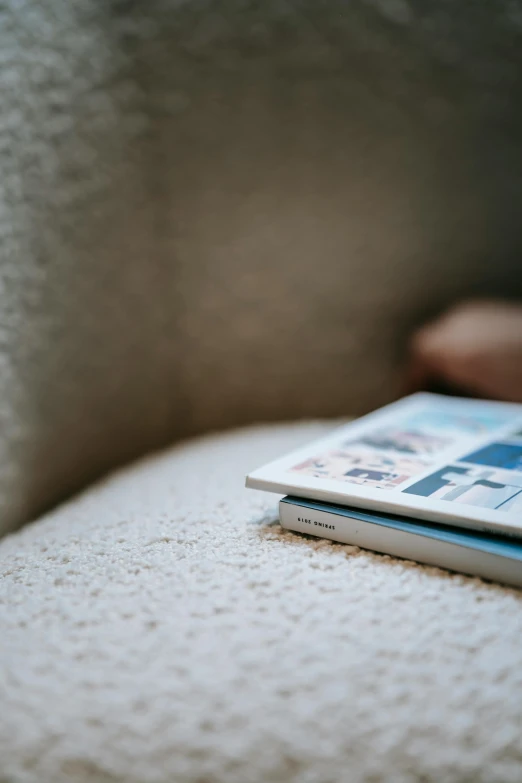 a book sitting on top of a white couch, unsplash, private press, magazine scraps, blue soft details, contemplating, sitting on the floor