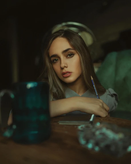 a woman sitting at a table with a blue mug, inspired by Elsa Bleda, trending on pexels, hyperrealism, pouty face, holding pencil, high quality photo, handsome girl