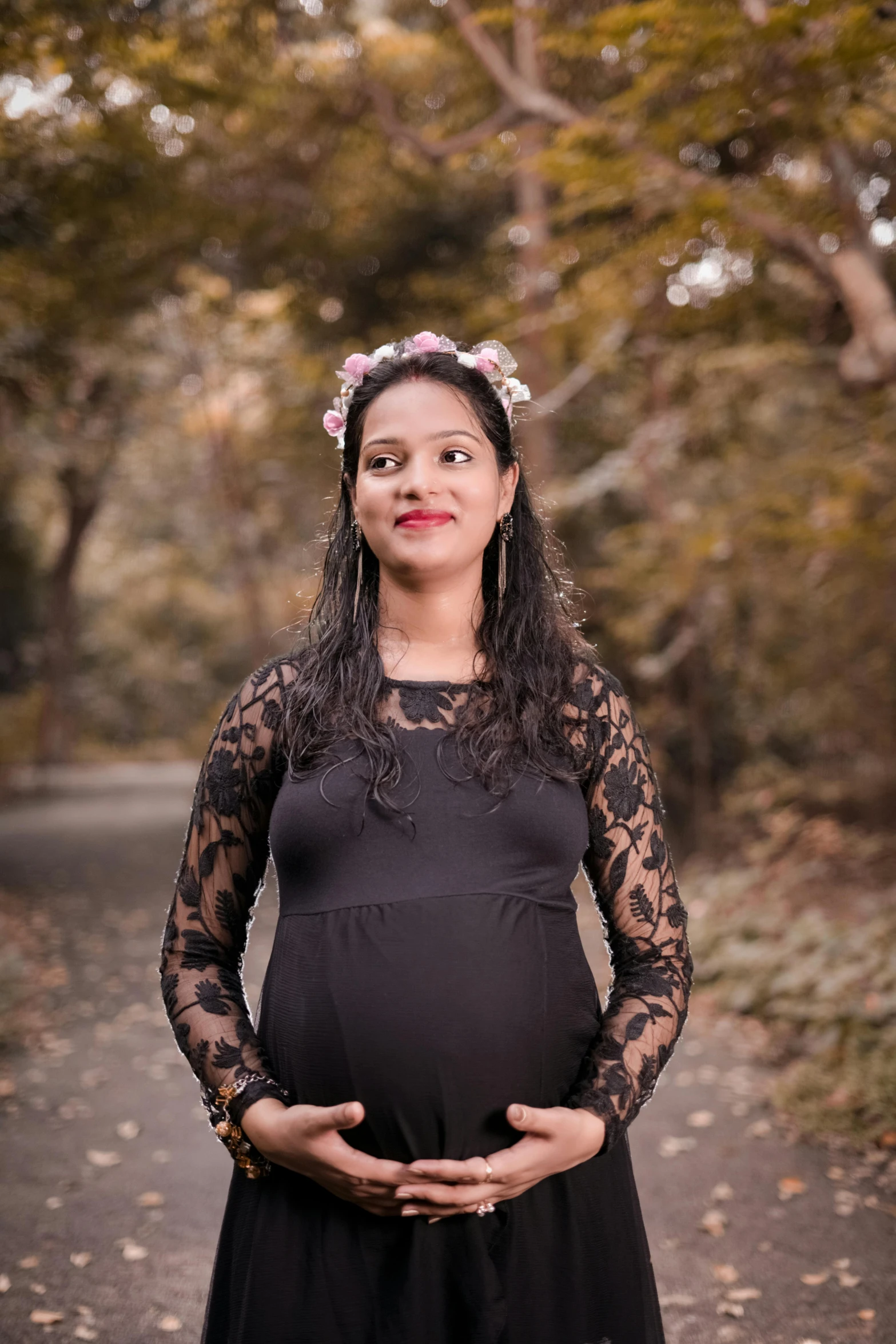 a pregnant woman standing in the middle of a road, an album cover, pexels contest winner, wearing a floral crown, candid!! dark background, with a happy expression, in a park