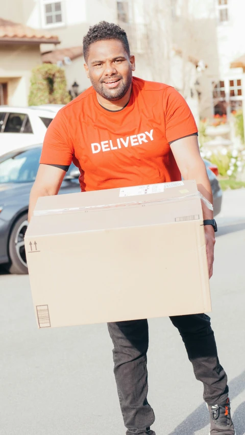 a man in an orange shirt is carrying a box, pexels contest winner, hurufiyya, wearing pants and a t-shirt, 15081959 21121991 01012000 4k, label, without text