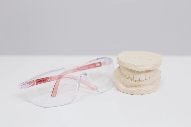 a pair of glasses sitting next to a dental model, white and pink, square jaw, skincare, white glasses