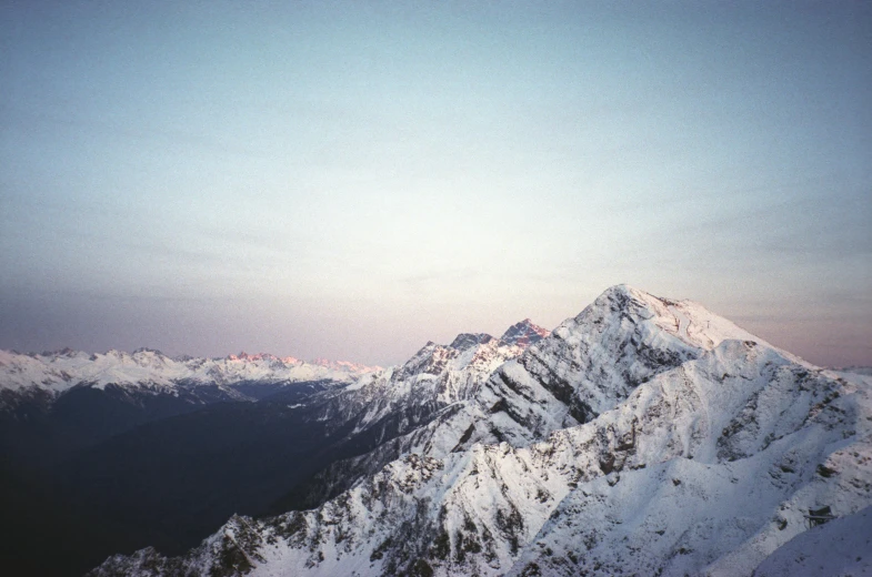 a person standing on top of a snow covered mountain, unsplash contest winner, minimalism, expired color film, dusk light, “ aerial view of a mountain, distant mountains lights photo