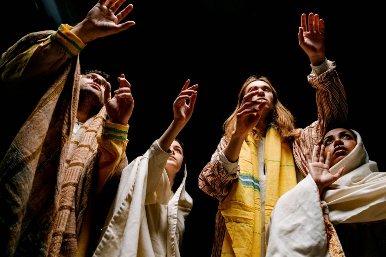 a group of people standing on top of a stage, by Nathalie Rattner, unsplash, hurufiyya, yellow robes, joseph and joseph, hands, production photo