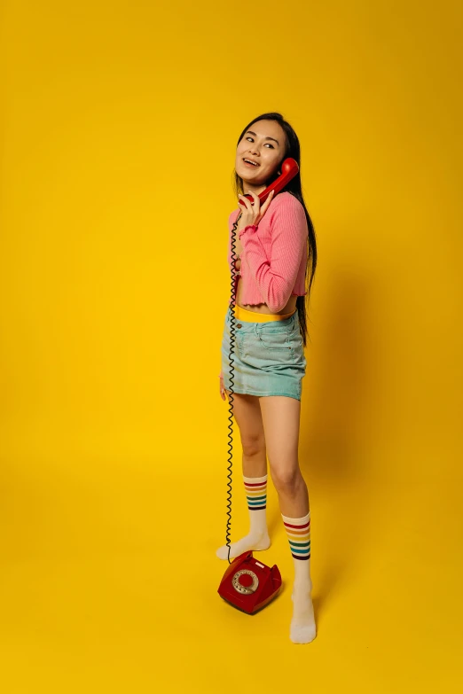 a woman standing next to a red phone, pink and yellow, wearing kneesocks, young teen, photo from a promo shoot