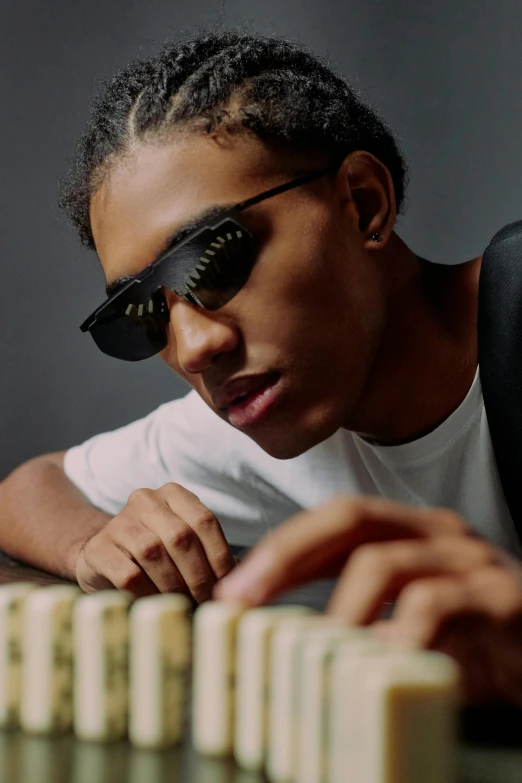 a man sitting at a table with dominos in front of him, inspired by Michael Ray Charles, trending on unsplash, visual art, black teenage boy, gold glasses, keyboardist, photo of a model