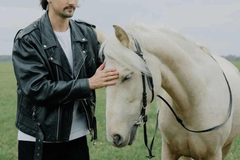 a man standing next to a white horse in a field, an album cover, by Emma Andijewska, trending on unsplash, leather jackets, hand on his cheek, avan jogia angel, photoshoot for skincare brand