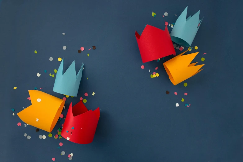 a couple of paper crowns sitting on top of a table, by Helen Stevenson, trending on unsplash, red yellow blue, party at midnight, graphic print, castles floating in mid air