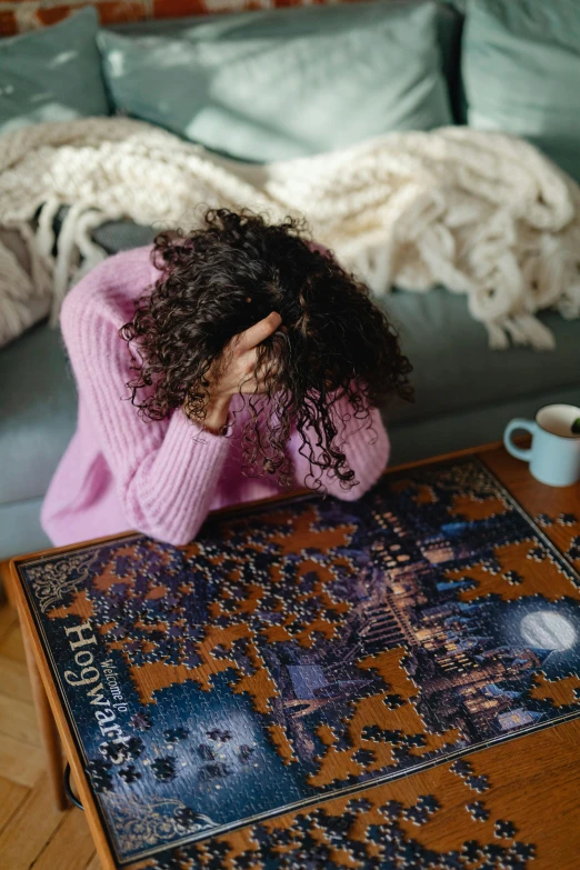 a woman sitting on a couch looking at a puzzle, a jigsaw puzzle, by Julia Pishtar, hurufiyya, facepalm, frizzy hair, cosy enchanted scene, board games on a table