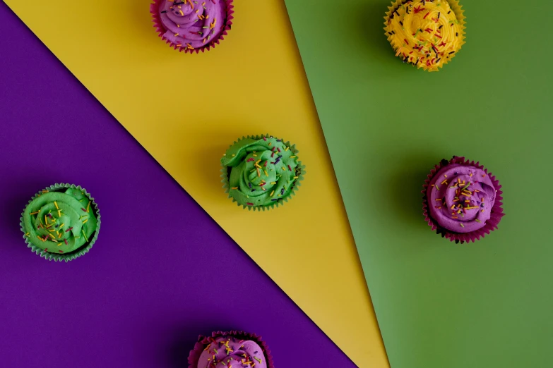a group of cupcakes sitting on top of a colorful surface, by Winona Nelson, trending on pexels, color field, yellow purple green black, background image, thumbnail, purple green color scheme