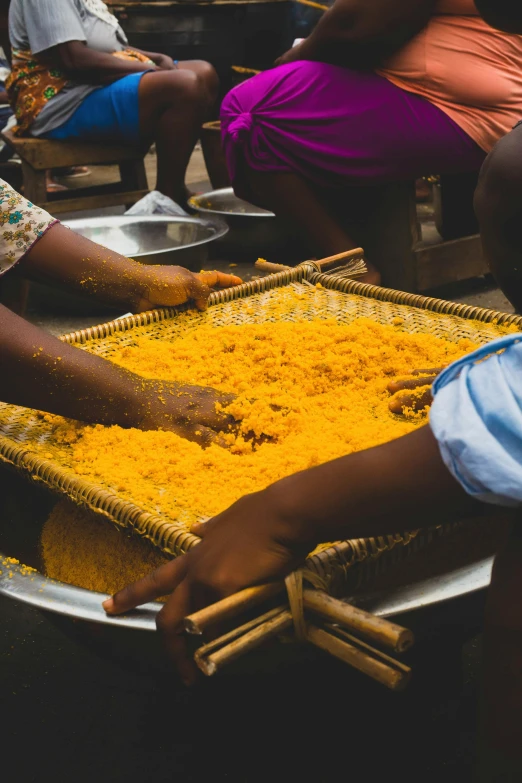 a group of people sitting around a tray of food, a silk screen, yellow orange, madagascar, spices, high-quality photo