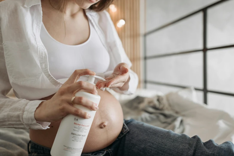 a woman sitting on a bed holding a bottle of lotion, a picture, trending on pexels, figuration libre, pregnant belly, with textured hair and skin, acupuncture treatment, on a white table