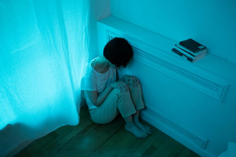 a woman sitting on the floor in front of a window, inspired by Elsa Bleda, blue lighting, rinko kawaichi, emotional pain, in small room