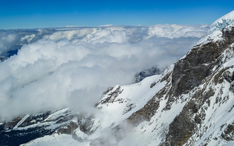 a man standing on top of a snow covered mountain, by Peter Churcher, pexels contest winner, hurufiyya, large white clouds, panoramic, high angle close up shot, lauterbrunnen valley