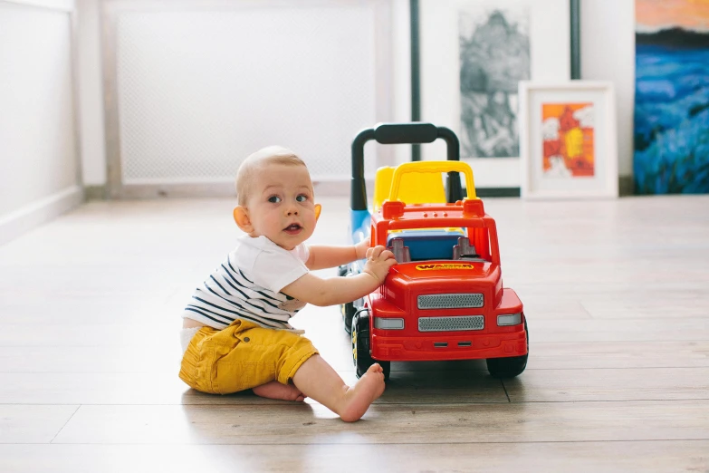 a baby sitting on the floor playing with a toy truck, pexels contest winner, red and yellow scheme, wearing a shirt and a jean, multi-part, small man