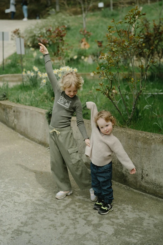 a couple of kids standing next to each other on a sidewalk, by Attila Meszlenyi, wearing cargo pants, around tree babies running, in a garden, late 2000’s