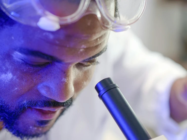 a man in a lab coat looking through a microscope, by Julian Allen, riyahd cassiem, holding a blue lightsaber, close-up photo, profile image