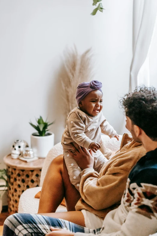 a man sitting on a couch holding a baby, pexels contest winner, renaissance, varying ethnicities, manuka, adorable design, she is happy