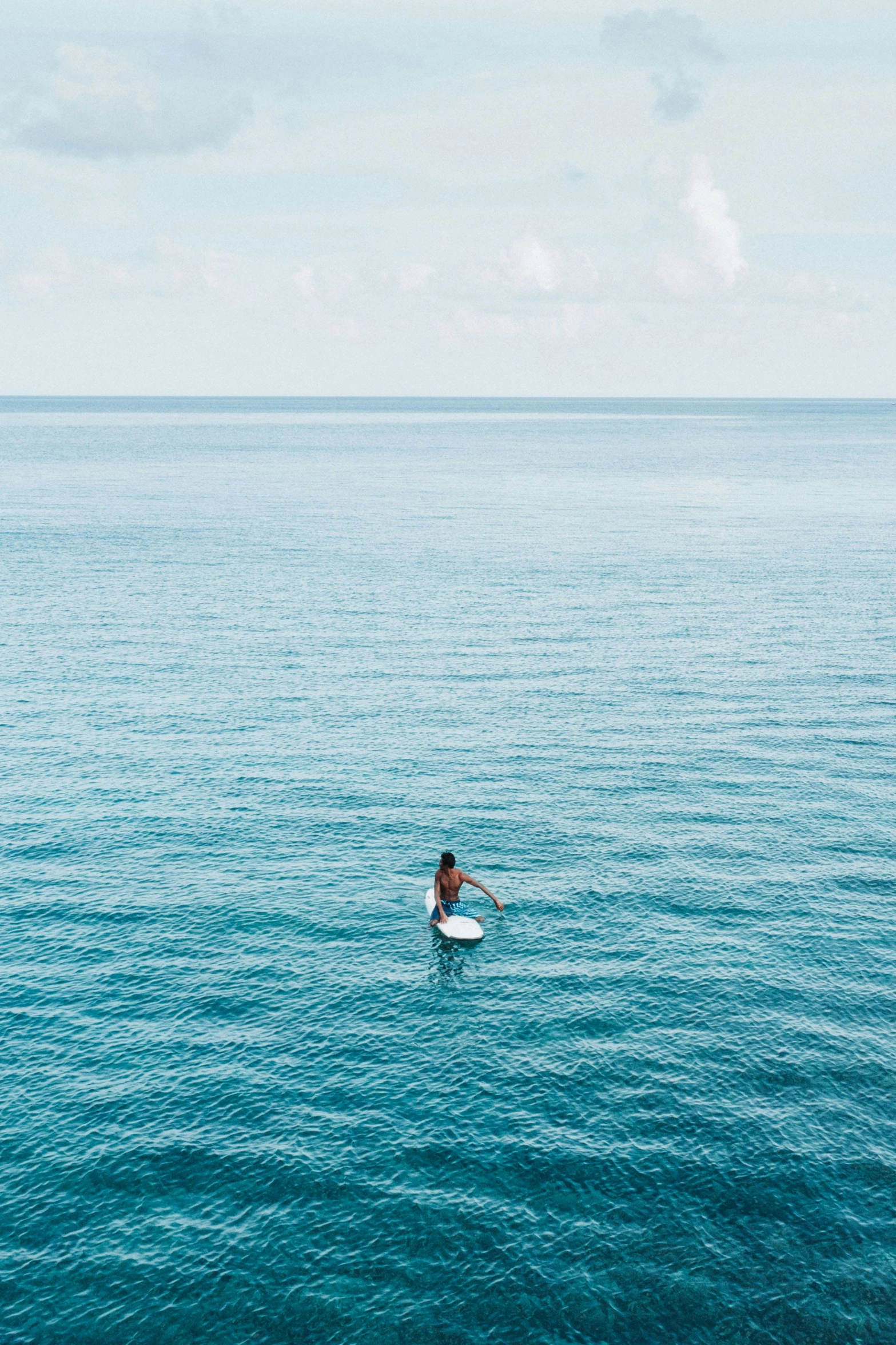 a person on a surfboard in the middle of the ocean, light blue water, overlooking the ocean, in the water