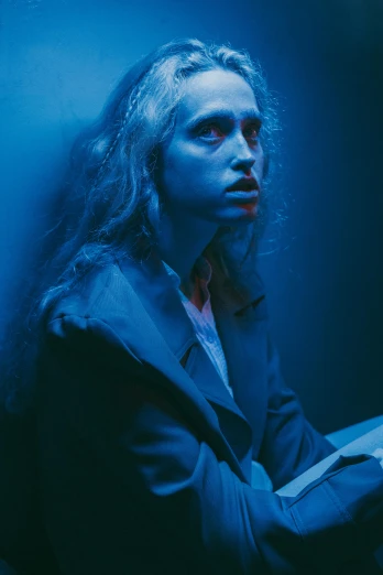 a woman holding a book in a dark room, an album cover, inspired by Elsa Bleda, neo-figurative, ((blue)), long glowing ethereal hair, movie filmstill, suspiria