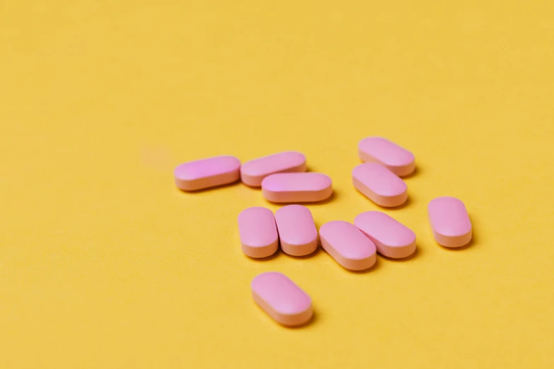 pink pills on a yellow background, by Rachel Reckitt, trending on pexels, on grey background, trans rights, pink skin, on a table