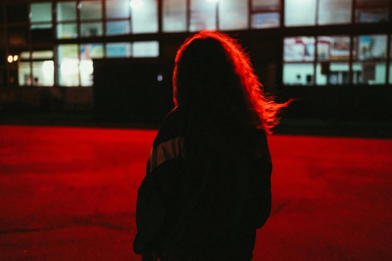 a person standing in front of a building at night, inspired by Elsa Bleda, antipodeans, long hair and red shirt, unsplash photography, black and red, standing in a parking lot