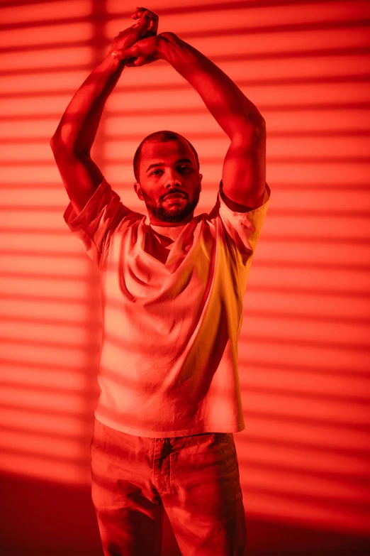 a man standing in front of a red wall, an album cover, inspired by Theo Constanté, orange and red lighting, pose(arms up + happy), jeffrey wright, standing under a beam of light