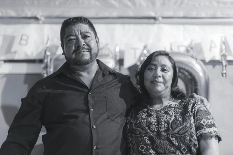 a man and a woman standing next to each other, a black and white photo, by Alejandro Obregón, community celebration, promo image, portrait image, family