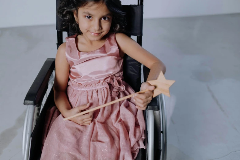 a little girl in a pink dress sitting in a wheel chair, pexels contest winner, hurufiyya, holding the elder wand, wearing a dress made of stars, award - winning details, accessible for the disabled