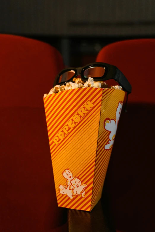 a popcorn box sitting on top of a red chair, a cartoon, file photo, glasses |, buffalo, inside view