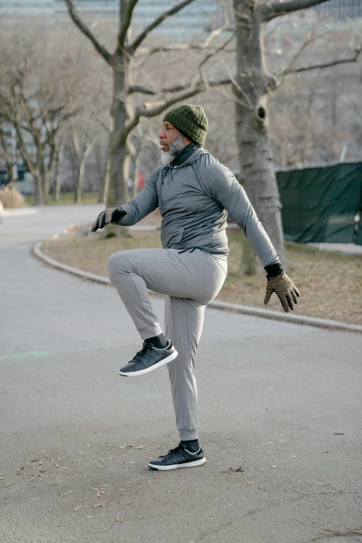 a man riding a skateboard down a street, inspired by Salomon van Abbé, happening, boxing stance, in the winter, at a park, grey