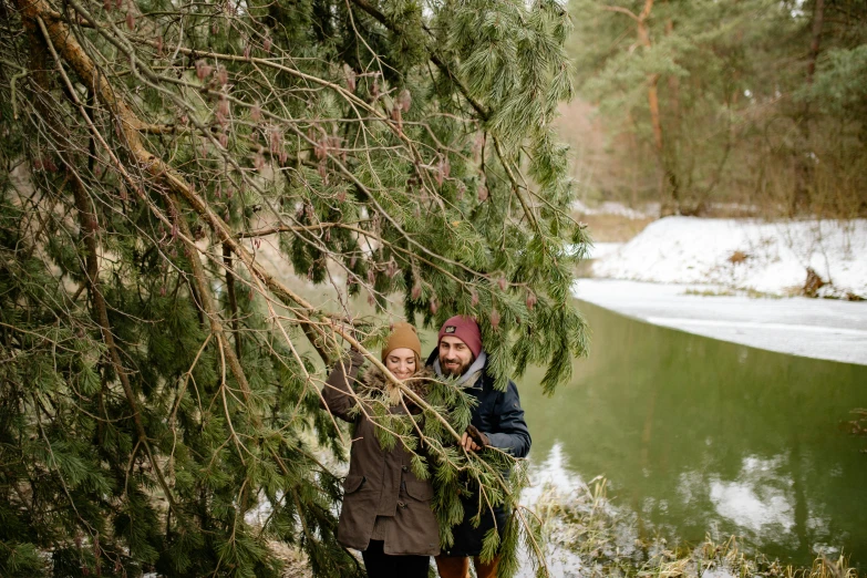a man and a woman standing next to a river, by Grytė Pintukaitė, pexels contest winner, hurufiyya, pine tree, outside winter landscape, avatar image, portrait image