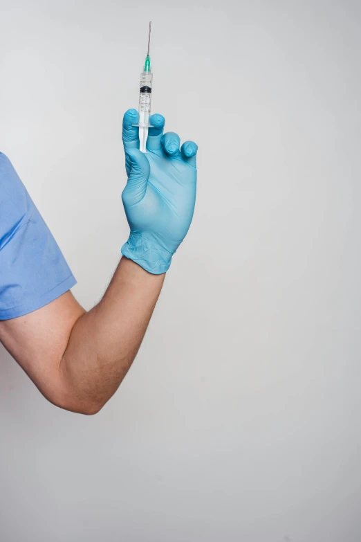 a man in a blue shirt is holding a syet, shutterstock, plasticien, holding a syringe, wearing gloves, plain background, ap news