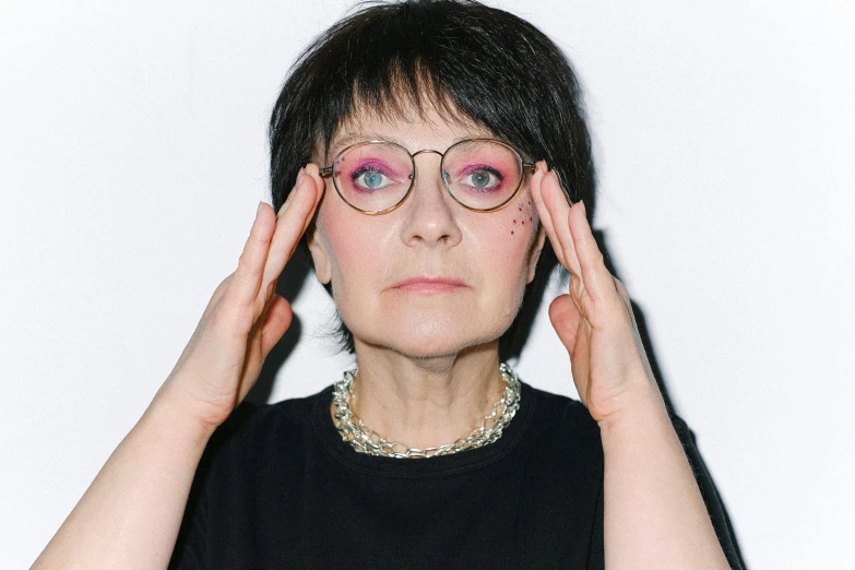 a woman with glasses holding her hands to her face, an album cover, by Leo Leuppi, pexels contest winner, tina belcher as a real person, vivienne westwood, declan mckenna, high quality photo